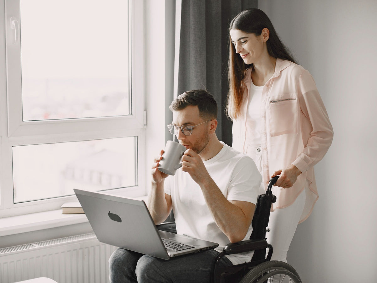 Wheelchair user receiving support while working on a laptop at home